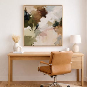 Op de afbeelding: Een abstract schilderij in een houten lijst hangt boven een houten bureau. Het schilderij toont een mix van kleuren, waaronder bruin, groen en wit. Een bruin lederen bureaustoel staat voor het bureau. Een witte lamp en vaas staan op het bureau.