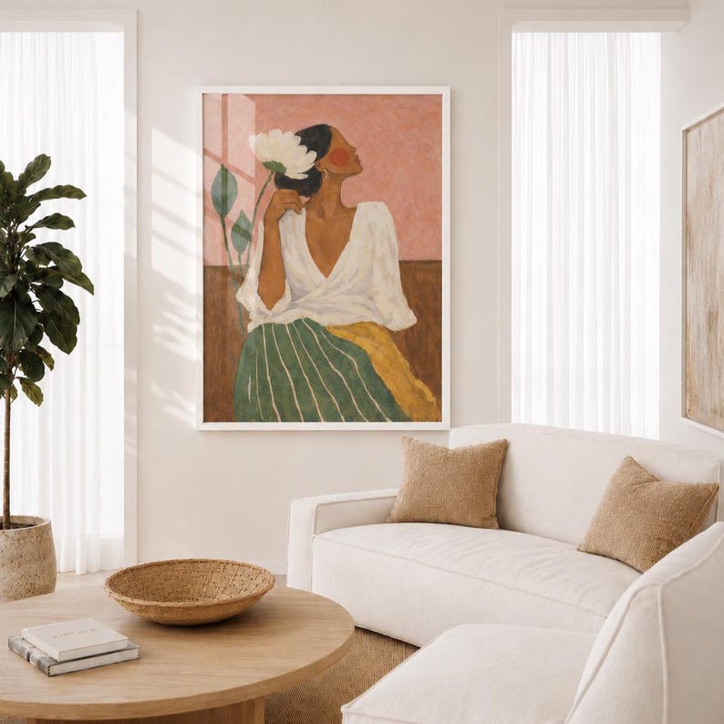 May include: A framed wall art print featuring a stylized illustration of a figure with dark hair wearing a white V-neck top and a green and yellow striped skirt, holding a large white flower against a muted pink and brown background.