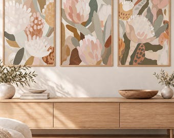 May include: A set of three framed wall art prints featuring abstract floral illustrations in a muted color palette of soft pink, sage green, terracotta, and cream. Each rectangular print displays stylized protea flowers and organic foliage shapes.