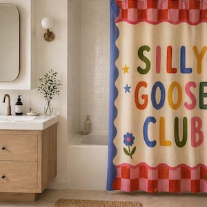 May include: A shower curtain featuring a cream-colored center with the text SILLY GOOSE CLUB in multicolored letters. The design includes a blue scalloped border, small star and flower icons, and a pink and red checkered pattern at the top and bottom.