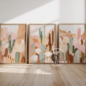 Può includere: Tre stampe artistiche astratte incorniciate con paesaggi di cactus del deserto in morbidi colori pastello. L'opera d'arte comprende sfumature di rosa, pesca, verde e marrone, con una silhouette di cavallo in una stampa. Le cornici sono di colore legno chiaro.
