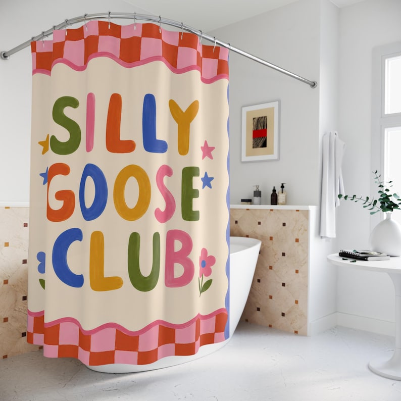 May include: A shower curtain featuring a cream-colored center with the text SILLY GOOSE CLUB in multicolored bubble letters. The design includes small star and flower accents, framed by a wavy pink border and a red and pink checkered pattern.