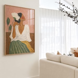 May include: A framed wall art print featuring a painting of a person with dark hair wearing a white wrap top and a green and yellow striped skirt. The person holds a large white flower against a pink and brown background with green leaves.