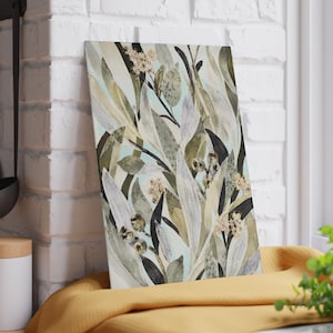 Könnte beinhalten: Ein rechteckiges Glasschneidebrett mit einem botanischen Aquarell-Druck, der längliche Blätter in Olivgrün, Salbei und Dunkelgrau auf hellblauem Hintergrund zeigt, akzentuiert durch kleine beige Blütencluster.