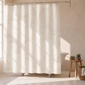 May include: A shower curtain featuring a large-scale, repeating line-art pattern of abstract, fan-shaped floral motifs in a soft beige color against a cream-colored background, suspended from a metal rod with integrated curtain rings.