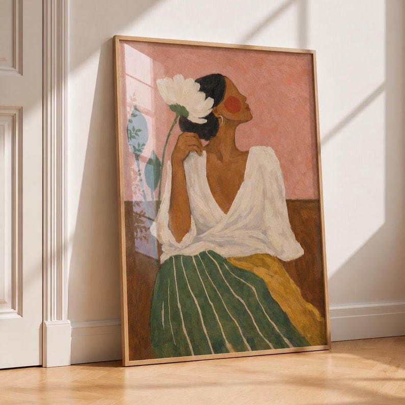 May include: A framed wall art print featuring a painting of a person with dark hair in a white wrap top and a green and yellow striped skirt. The person holds a large white flower near their face against a pink and brown background.