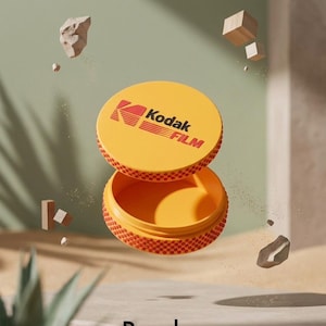May include: Open yellow container with the Kodak Film logo on the lid. The container is round with a textured, dotted pattern on the rim. The word "Render" is at the bottom of the image.