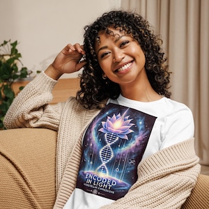 Könnte beinhalten: Weißes T-Shirt mit einem farbenfrohen Grafikdesign, das eine Lotusblume, eine DNA-Doppelhelix und einen Galaxie-Hintergrund zeigt. Der Text "Encoded in Light" und "Interstellar Expressions" ist auf dem Shirt aufgedruckt.