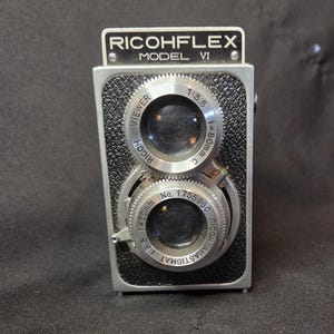 May include: A vintage Ricohflex Model VI twin-lens reflex camera with a black textured body and silver metal accents. The top lens is labeled Ricoh Viewer 1:3.5 f=80mm, and the bottom lens is labeled Ricoh Anastigmat 1:3.5 f=80mm No. 175596C.