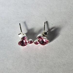 Op de afbeelding: Zilveren oorstekers met drie roze edelstenen. De oorbellen hebben een pin en een vlindersluiting. De edelstenen zijn helderroze en voegen elegantie toe. Sieraden voor vrouwen.