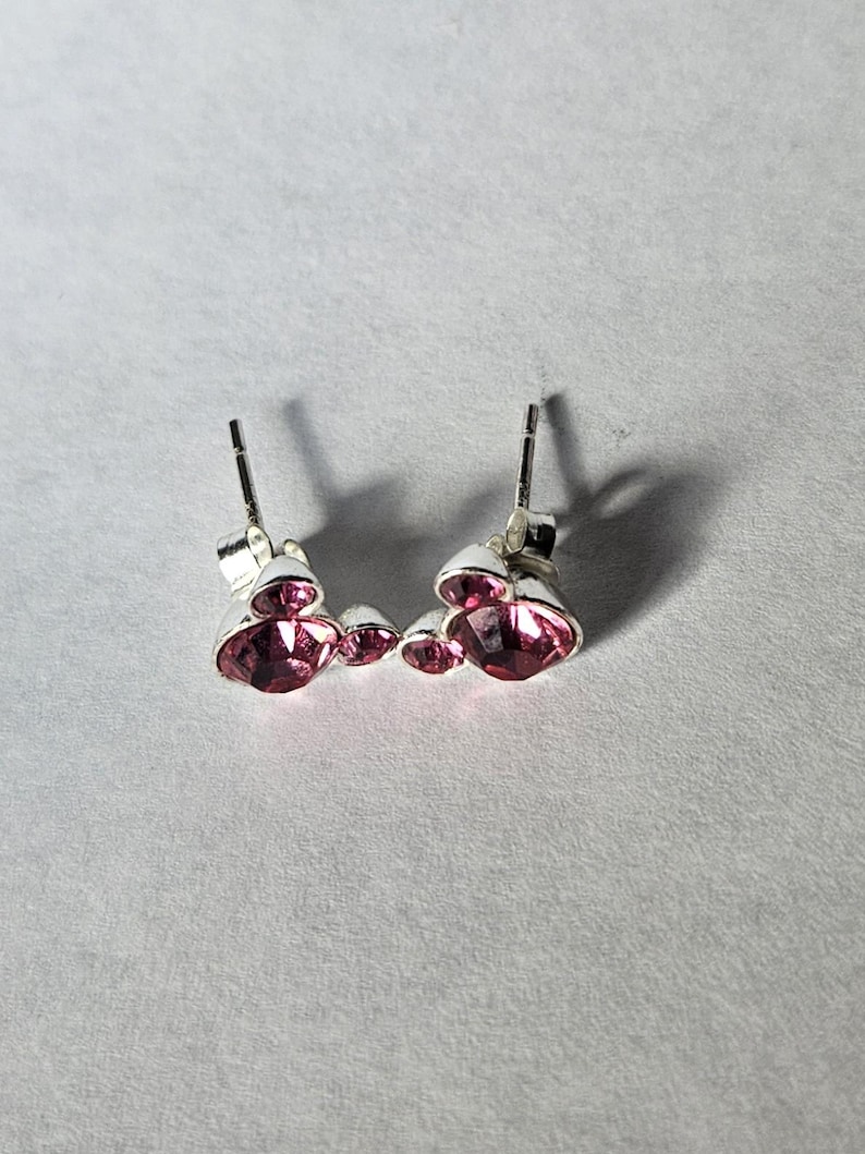 Op de afbeelding: Zilveren oorstekers met drie roze edelstenen. De oorbellen hebben een pin en een vlindersluiting. De edelstenen zijn helderroze en voegen elegantie toe. Sieraden voor vrouwen.