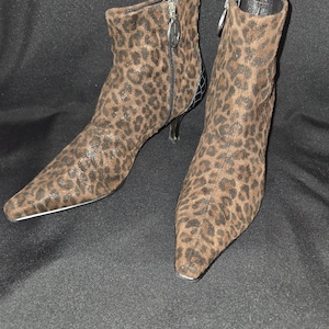 May include: A pair of ankle boots with a leopard print pattern. The boots have pointed toes, stiletto heels, and zippers on the sides. The heels are approximately 3 inches high.
