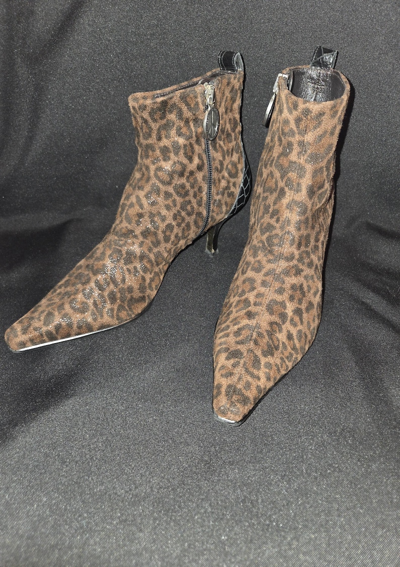 May include: A pair of ankle boots with a leopard print pattern. The boots have pointed toes, stiletto heels, and zippers on the sides. The heels are approximately 3 inches high.