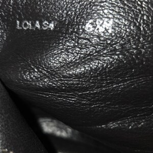May include: Close-up of a black leather shoe interior. The text "LOLA S4" is visible, along with the size "6M". The brand name "DONALD J PLINER" is also present. The leather has a textured appearance.