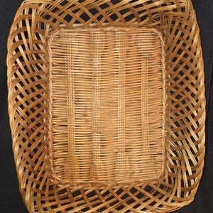 May include: A square woven basket with a light brown color. The basket has a rectangular base with a woven pattern and a decorative woven border. The basket is made of natural materials and is suitable for storage or display.