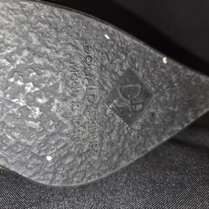 May include: Close-up of a black shoe sole with a textured surface. The sole has the brand name "DONALD J. PLINER" and "made in Spain" printed on it, along with a logo.