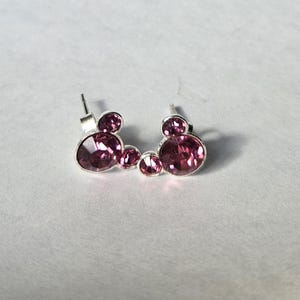 Op de afbeelding: Een paar oorstekers met een ontwerp van drie cirkels met roze edelstenen. De oorbellen hebben een zilverkleurige metalen zetting en een steker sluiting. De edelstenen hebben een levendige roze kleur.