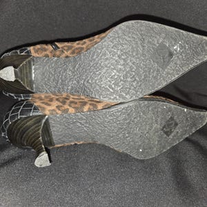 May include: A pair of women's ankle boots with a pointed toe and a small heel. The upper part of the boot features a brown and black leopard print pattern. The heel and back of the boot are black with a textured design.