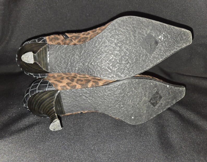 May include: A pair of women's ankle boots with a pointed toe and a small heel. The upper part of the boot features a brown and black leopard print pattern. The heel and back of the boot are black with a textured design.