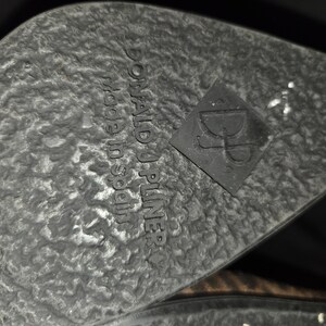 May include: Close-up of a shoe sole with a textured, dark gray surface. The words "DONALD J PLINER made in Spain" are embossed on the sole. A black square with the letters "DJ" is also visible.