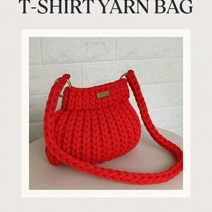 Pode incluir: Uma bolsa de fio de camiseta vermelha brilhante, feita &agrave; m&atilde;o, com uma al&ccedil;a tran&ccedil;ada e argolas douradas. A bolsa tem um design texturizado e canelado e uma pequena etiqueta retangular. O texto "CROCHET PATTERN" e "T-SHIRT YARN BAG" s&atilde;o exibidos.