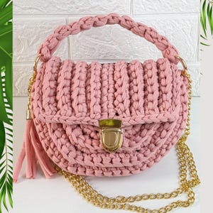 May include: A pink crocheted handbag with a gold chain strap and a gold clasp. The bag has a tassel on the side.
