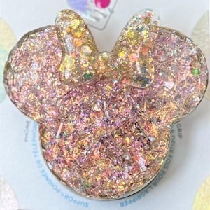 Op de afbeelding: Een roze en gouden glitter PopSocket telefoon grip met een Minnie Mouse hoofd ontwerp. De PopSocket is verpakt op een witte kaart met het PopSockets logo en de tekst "PopGrip".