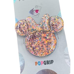 Op de afbeelding: Een glitterende PopSockets PopGrip in de vorm van een strik en oren. De PopGrip is gevuld met iriserende glitter en is bevestigd aan een grijze achtergrondkaart met de logo's PopSockets en PopGrip.