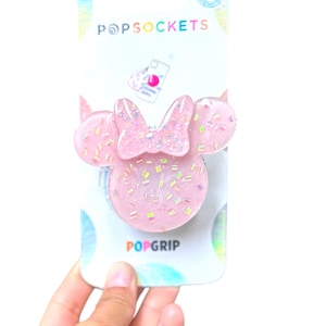 Puede incluir: PopSockets PopGrip rosa con diseño de Minnie Mouse. El accesorio para teléfono tiene forma de lazo y orejas con detalles de purpurina. El embalaje dice "POPSOCKETS" y "POPGRIP".