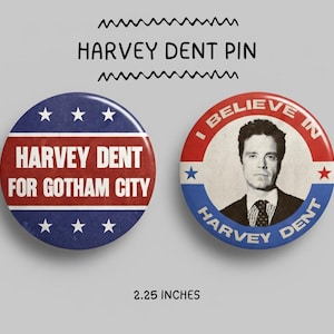 May include: Two round Harvey Dent pins. One pin has a red and white stripe design with the text "HARVEY DENT FOR GOTHAM CITY" and stars. The other pin has a portrait of a man and the text "I BELIEVE IN HARVEY DENT". Each pin is 2.25 inches in diameter.