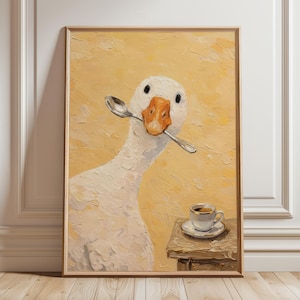 Könnte beinhalten: Gerahmter Kunstdruck einer weißen Gans mit einem Löffel im Schnabel, vor gelbem Hintergrund. Ein kleiner Tisch trägt eine Tasse Kaffee. Das Kunstwerk hat ein strukturiertes, gemaltes Aussehen.