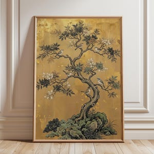 May include: A framed vertical wall art print featuring a stylized tree with dark branches, green leaves, and white flowers. Several small birds are perched on the branches. The background is a textured, metallic gold color with a rocky base.
