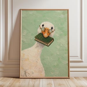 Puede incluir: Impresión artística enmarcada que presenta una ilustración de un ganso blanco con gafas redondas y un libro verde en el pico. El fondo es verde claro texturizado, con un marco de madera.