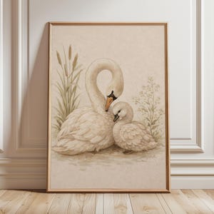 May include: A framed watercolor print featuring two white swans, one adult and one cygnet, nestled together. The artwork has a soft, muted color palette with touches of green and brown, evoking a sense of tranquility and nature. The frame is a light brown color.