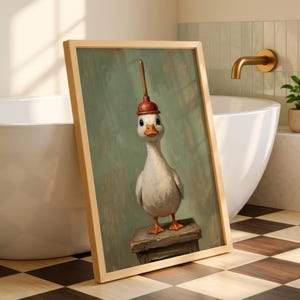 Puede incluir: Obra de arte enmarcada que presenta un ganso caprichoso con un sombrero de desatascador rojo. El ganso está de pie sobre un pequeño bloque de madera contra un fondo verde apagado. La obra se exhibe en un baño con una bañera blanca y un grifo dorado.