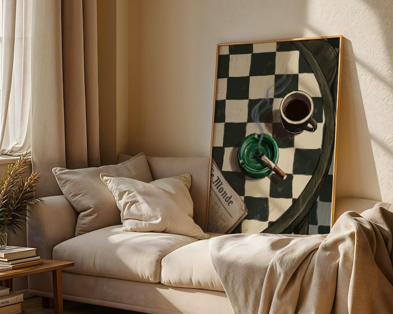 May include: A framed artwork depicts a still life with a cup of coffee, a lit cigar in a green ashtray, and a newspaper. The background features a black and white checkered pattern. The artwork is displayed above a beige sofa.