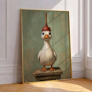 Op de afbeelding: Een ingelijste kunstprint met een eigenzinnige gans met een rode ontstopperhoed. De gans staat op een kleine houten kruk tegen een gedempte groene achtergrond. Het kunstwerk heeft een vintage, schilderachtige stijl, met een gouden lijst.