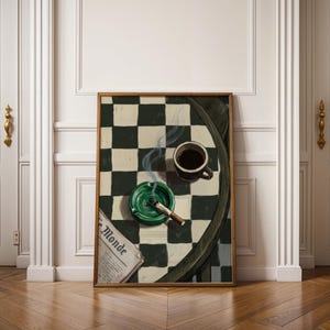May include: A framed artwork depicts a still life with a cup of coffee, a green ashtray with a lit cigarette, and a newspaper with the text "Le Monde" on a checkered table. The artwork is displayed in a room with white doors and a wooden floor.