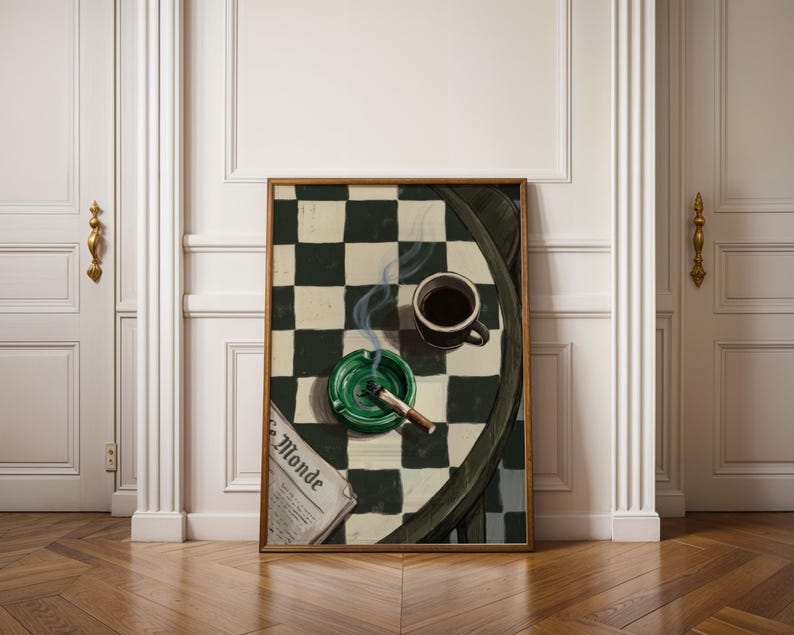 May include: A framed artwork depicts a still life with a cup of coffee, a green ashtray with a lit cigarette, and a newspaper with the text "Le Monde" on a checkered table. The artwork is displayed in a room with white doors and a wooden floor.