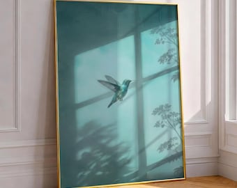Op de afbeelding: Een rechthoekige wandkunstprint in een dunne gouden lijst met een afbeelding in groenblauwe tinten van een vliegende kolibrie. Het kunstwerk toont de schaduw van een raamkozijn en silhouetten van bladeren die op het oppervlak vallen.