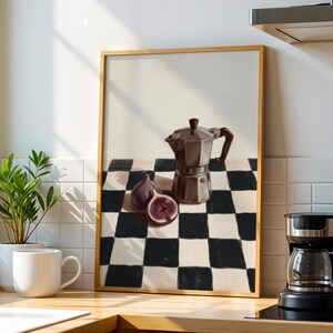 May include: A framed print featuring a still life with a brown stovetop espresso maker, figs, and a black and white checkered pattern. A coffee maker and a mug are in the foreground.