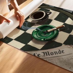 May include: A rolled-up print featuring a black and white checkered pattern, a green ashtray with a lit cigarette, a black coffee cup, and a newspaper with the text "Le Monde". The print is being unrolled on a wooden surface.