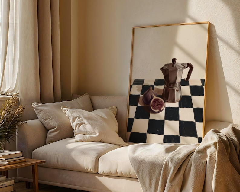 May include: A framed still life painting featuring a dark brown stovetop espresso maker, figs, and a black and white checkered pattern. The painting is displayed on a beige wall above a beige sofa.