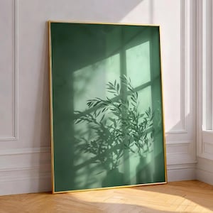 May include: A rectangular wall art print featuring a deep forest green background with a soft, blurred shadow of leafy plant branches cast across the surface. The artwork is encased in a thin, metallic gold frame with sharp, clean edges.