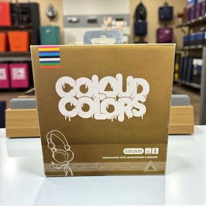 May include: A gold-colored box with the words "COLOUD COLORS" in white graffiti-style lettering. The box features a graphic of headphones and the text "HEADPHONES WITH MICROPHONE & REMOTE". A colorful stripe design is at the top.