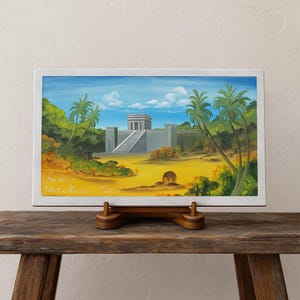 May include: A rectangular painting of a temple scene with a blue sky and palm trees. The artwork is displayed on a wooden easel. The painting features a temple with a staircase, surrounded by lush greenery and a yellow landscape.