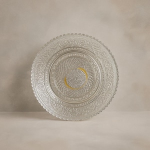 Könnte beinhalten: Dekorative Platte aus klarem Glas mit einem aufwendigen geprägten Blumen- und Wirbeldesign. Die Platte hat einen gewellten Rand und einen gelben Mittelakzent. Geeignet zum Servieren oder Ausstellen.