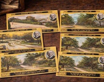 Op de afbeelding: Een verzameling vintage ansichtkaarten met landschappen van Lover's Lane en andere locaties. Elke kaart heeft een portret van een man en tekst. De kaarten zijn gerangschikt op een houten oppervlak.
