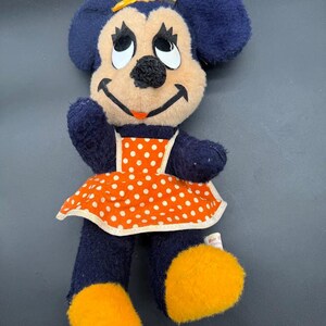 May include: A vintage plush toy of Minnie Mouse wearing a blue dress with orange and white polka dots and a yellow bow. The toy has a yellow bow and yellow shoes.