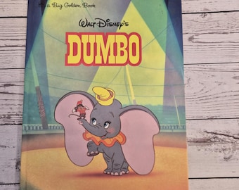 May include: A vintage "Big Golden Book" titled "Walt Disney's Dumbo." The cover features a colorful illustration of Dumbo the elephant in a circus setting, with a small figure perched on his trunk. The book has a blue background.